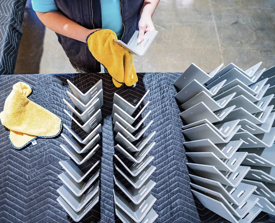 A gloved worker inspecting clear anodized aluminum angle brackets after finishing